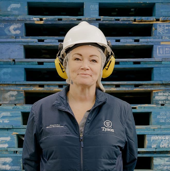 Tyson employee with a hard hat and noise protection device in front of a wall of pallets